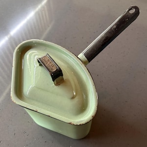 Op de afbeelding: Een groene emaille pan met een zwarte handgreep. De pan heeft een deksel met een zwarte handgreep en de tekst "W.P.G.I.  FIRE-KING" erop.