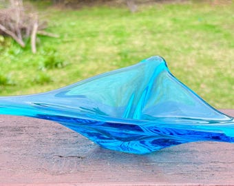 May include: A blue glass bowl with a unique, abstract design. The bowl is made of hand-blown glass and has a wavy, organic shape.