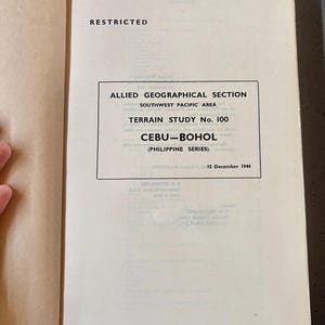 Può includere: Libro aperto con la parola "RESTRICTED" in alto. Il testo "ALLIED GEOGRAPHICAL SECTION" e "TERRAIN STUDY No. 100" sono visibili. Lo studio riguarda Cebu-Bohol, Filippine, datato 15 dicembre 1944.