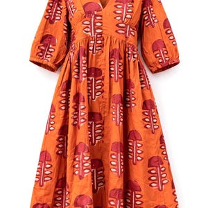 May include: An orange dress with a V-neck and elbow-length sleeves. The dress features a repeating pattern of red and white abstract shapes. The dress is made of a lightweight fabric and has a gathered waist.