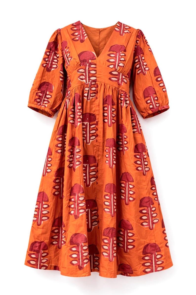 May include: An orange dress with a V-neck and elbow-length sleeves. The dress features a repeating pattern of red and white abstract shapes. The dress is made of a lightweight fabric and has a gathered waist.