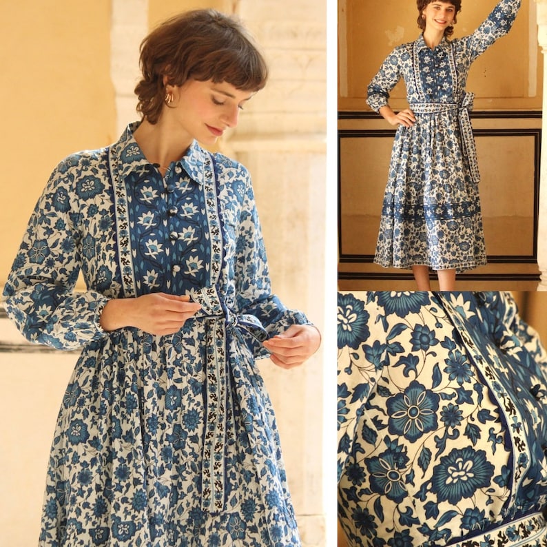 May include: A long-sleeved dress with a white background and a blue floral pattern. The dress has a collar and a tie at the waist. The dress is made of cotton and is perfect for a summer day.