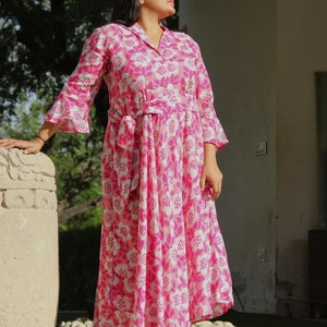 May include: A pink and white floral print maxi dress with a tie waist and bell sleeves. The dress is made of a lightweight fabric and is perfect for warm weather.