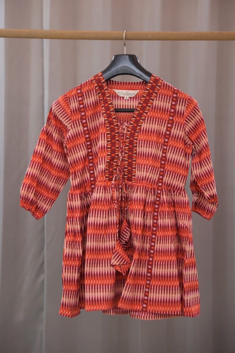 Op de afbeelding: Een rood-wit gebloemde jurk met een V-hals en een strik aan de voorkant. De jurk heeft een label met de tekst "Occasions".