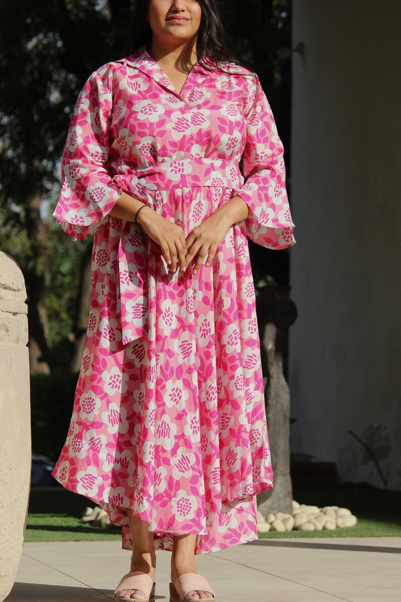 May include: A pink and white floral print dress with a long sleeve and a tie at the waist.