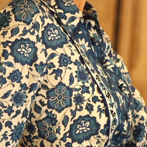 May include: A white shirt with a blue floral pattern. The shirt has a collar and a button-up front. The shirt is made of a lightweight fabric and has a relaxed fit.