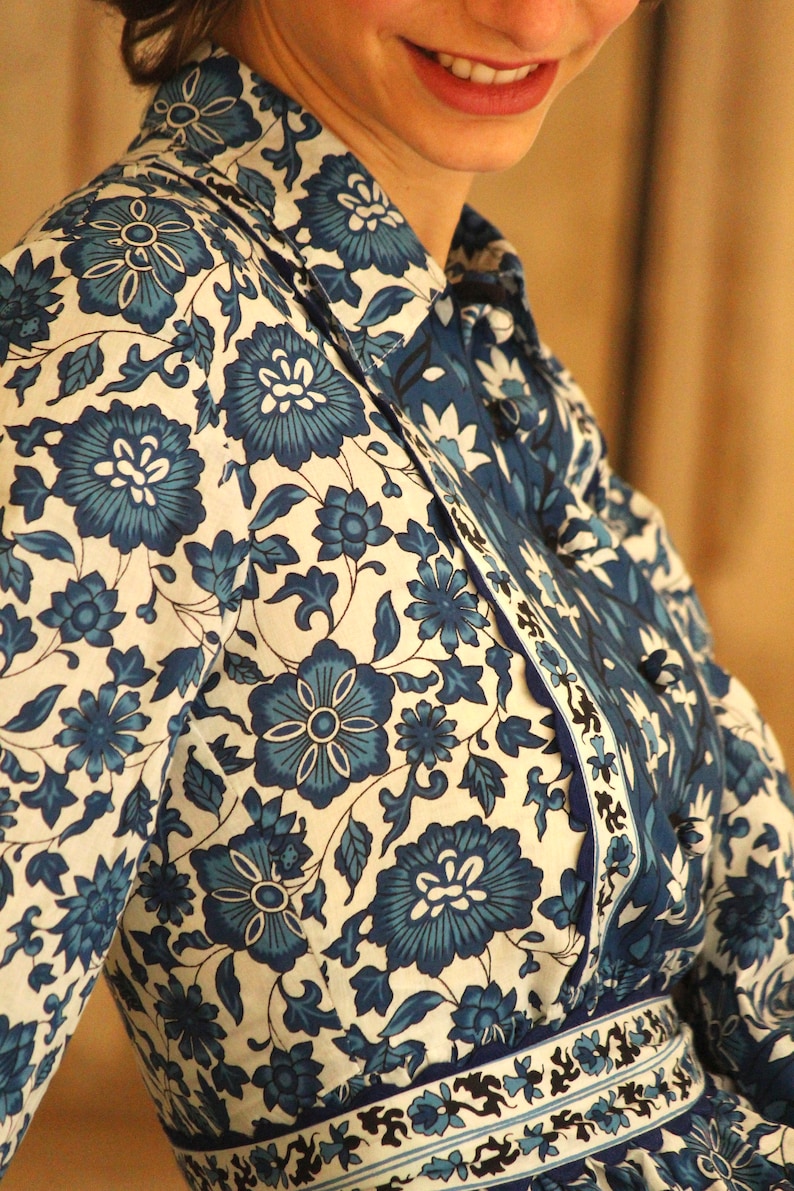 May include: A white shirt with a blue floral pattern. The shirt has a collar and a button-up front. The shirt is made of a lightweight fabric and has a relaxed fit.