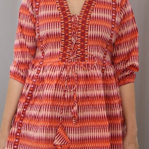 Op de afbeelding: Een rood, oranje en wit gepatroneerde tuniek met een vetersluiting aan de halslijn. De tuniek heeft een losse pasvorm en 3/4 mouwen.