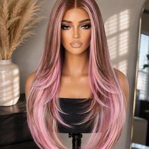 May include: A long, straight synthetic wig featuring a center part with a blend of light brown and dark brown hair tones, accented by prominent, face-framing streaks of pastel pink throughout the layers and ends of the hair.
