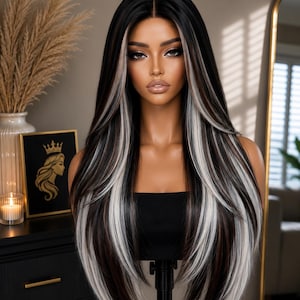 May include: A long, straight wig featuring a dark brown base color with prominent, bright white highlights framing the face and distributed throughout the lengths. The hair is styled with a center part and layered ends, displayed on a mannequin head.