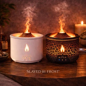Puede incluir: Dos difusores de aromaterapia con efecto llama, uno blanco y otro negro con un patrón agrietado. Ambos tienen un icono de llama y el texto "SLAYED BY FROST". Los difusores están sobre una superficie de madera.