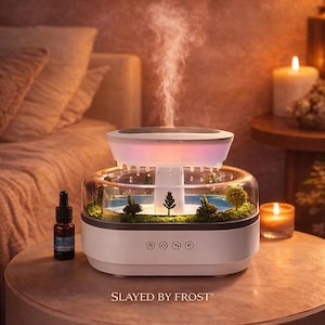 Può includere: Un diffusore di pioggia forestale rilassante bianco e trasparente con una scena di foresta in miniatura all'interno. Il diffusore ha una parte superiore che emette vapore ed è circondato da un'atmosfera calda e accogliente. Il testo "Relaxing Forest Rain Diffuser" è in alto.