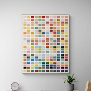May include: A framed abstract art print with a grid of colorful squares in various shades of red, orange, yellow, green, blue, purple, pink, brown, and gray. The print is hanging on a white wall above a wooden desk with a clock and a chair.