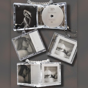 Puede incluir: Llaveros de CD de plástico transparente con imágenes en blanco y negro y un CD. Los llaveros tienen una cadena en forma de corazón y una cadena de bolas plateada. El CD es plateado con el texto "The Manuscript" y "Taylor Swift".