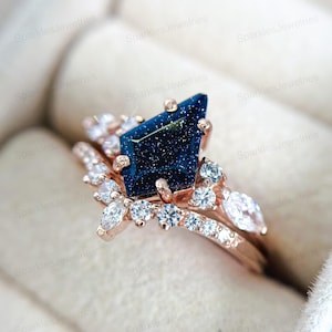 Puede incluir: Un anillo de compromiso de oro rosa con una piedra preciosa azul y una banda de piedras blancas más pequeñas.
