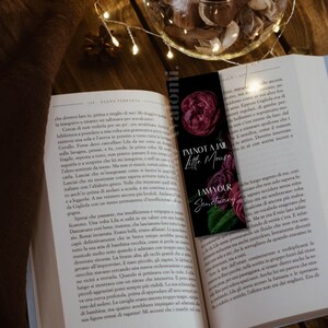 K&ouml;nnte beinhalten: Ein schwarzer Lesezeichen mit dem Text "I'm not a jail little mouse, I am your sanctuary" und Illustrationen von dunkelroten Rosen. Das Lesezeichen befindet sich in einem offenen Buch mit Text, mit Lichterketten und einer dekorativen Schale im Hintergrund.