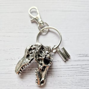 May include: Silver dinosaur skull keychain with a silver letter M charm attached to a silver key ring.