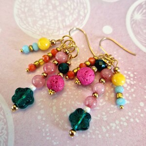 Op de afbeelding: Een paar gouden oorhangers met roze, gele, groene en oranje kralen. De oorhangers hebben een bloemvormige kraal aan de onderkant.