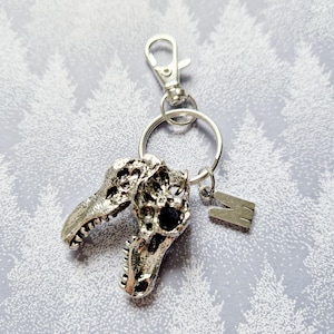 May include: Silver dinosaur skull keychain with a silver letter M charm attached to a silver key ring.