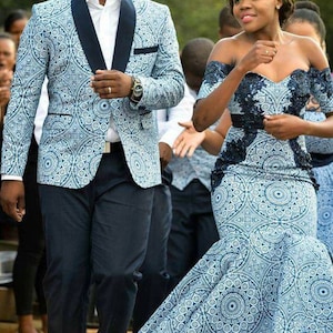 May include: A couple in matching blue and white patterned outfits. The man is wearing a blazer and the woman is wearing a dress with a lace bodice. They are both smiling and walking towards the camera.