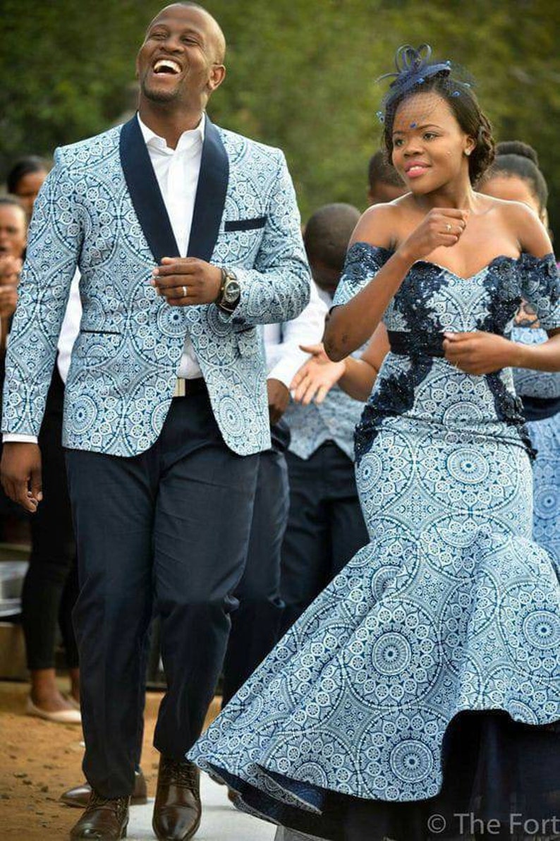 May include: A couple in matching blue and white patterned outfits. The man is wearing a blazer and the woman is wearing a dress with a lace bodice. They are both smiling and walking towards the camera.