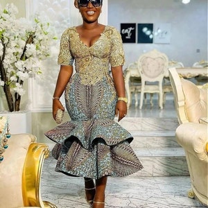 Pode incluir: Uma mulher vestindo um vestido estampado em dourado e azul com uma saia rodada. Ela est&aacute; usando &oacute;culos de sol e segurando uma pequena carteira.