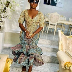 Pode incluir: Uma mulher vestindo um vestido estampado em dourado e azul com uma saia rodada. Ela est&aacute; usando &oacute;culos de sol e tem o cabelo puxado para tr&aacute;s.