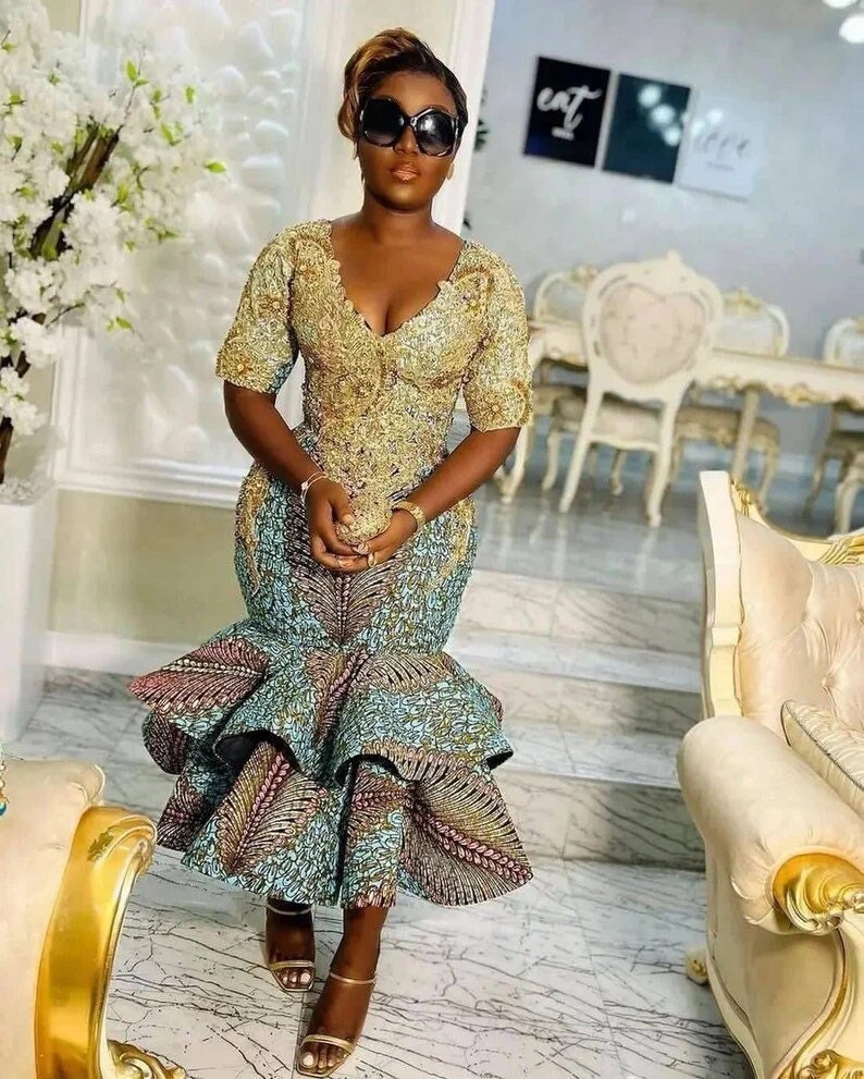 Pode incluir: Uma mulher vestindo um vestido estampado em dourado e azul com uma saia rodada. Ela est&aacute; usando &oacute;culos de sol e tem o cabelo puxado para tr&aacute;s.