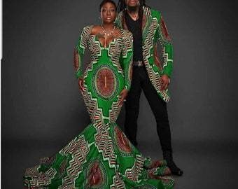 May include: A couple wearing matching green and brown patterned outfits. The woman is wearing a long-sleeved dress with a mermaid skirt. The man is wearing a long-sleeved shirt and a blazer.