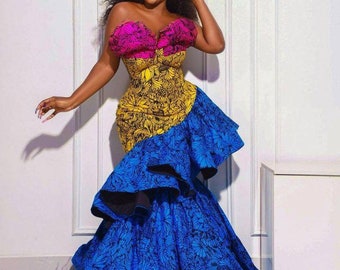 May include: A woman wearing a strapless dress with a pink, yellow, and blue floral print. The dress has a fitted bodice and a flowing skirt with ruffles.