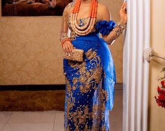 Puede incluir: Una mujer con un atuendo tradicional nigeriano azul y dorado con un collar de cuentas de coral y una corona de flores.
