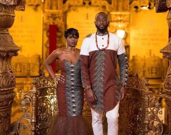 May include: A couple wearing matching brown and white patterned outfits with geometric designs. The woman is wearing a strapless dress with a brown tulle skirt. The man is wearing a long-sleeved shirt with white pants. They are standing in front of a gold-colored ornate background.