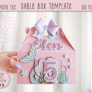 Könnte beinhalten: Rosa Gable-Box-Vorlage mit Meerjungfrauen-Motiv. Die Box zeigt eine Meerjungfrauenschwanz, die Zahl 5 und den Namen "Elen" in Glitzer. Eine hellviolette Schleife und türkisfarbene Akzente zieren die Oberseite. Der Text "Digital File" und "SVG File" sind sichtbar.