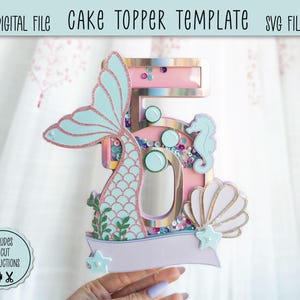 Può includere: Un modello di decorazione per torta a tema sirena con il numero 5. Il topper presenta una coda di sirena azzurra, un cavalluccio marino e una conchiglia. Il design include il testo "DIGITAL FILE CAKE TOPPER TEMPLATE SVG FILE" e "INCLUDES CRICUT INSTRUCTIONS".