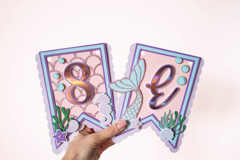 May include: A pink and purple mermaid-themed banner with the number "8" and the letter "E" in gold foil. The banner features a mermaid tail, seashells, and seaweed.