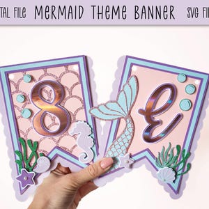 May include: A mermaid-themed banner with a pink background and purple and blue accents. The banner features the number 8, a mermaid tail, and sea-themed decorations. The banner is ideal for a birthday party.