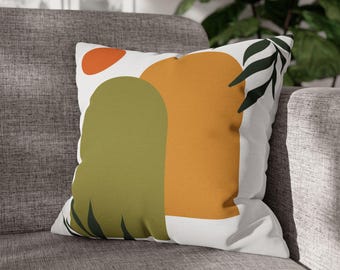 May include: A white throw pillow with an abstract design featuring green, orange, and red shapes. The design includes stylized leaves and a sun-like shape.