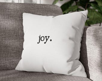 May include: White throw pillow with the word "joy" printed in black.