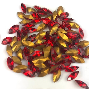 May include: A scattering of marquise-shaped rhinestones in red and gold. The red stones are faceted and appear to be made of glass or crystal. The gold stones have a metallic finish and a geometric design. These decorative stones are ideal for embellishing crafts.