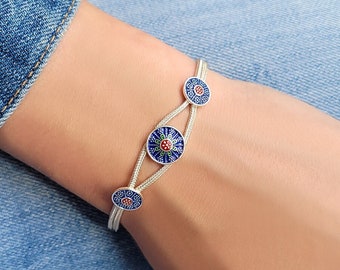 Puede incluir: Una pulsera de plata con tres abalorios redondos de esmalte azul y rojo. Los abalorios tienen un diseño floral.