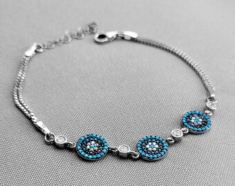 Pode incluir: Pulseira de prata com três pingentes de olho turco azul. Cada pingente é rodeado por pequenas pedras brancas.