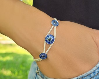 Puede incluir: Pulsera de plata con tres dijes de ojo turco azul y negro. La pulsera está hecha de una cadena delicada y tiene un diseño simple.