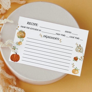 Peut inclure: Une carte de recette blanche sur le thème de la citrouille. La carte comporte des lignes pour écrire une recette, y compris le nom de la recette, les ingrédients, le temps de préparation, le temps de cuisson et le nombre de portions. La carte est décorée de petits dessins de citrouilles et de vignes.