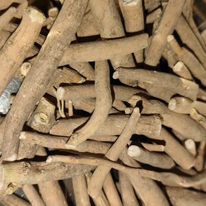 May include: Close-up of a pile of light brown, dried, and cut ashwagandha roots. The roots vary in size and shape, with some showing cut ends. The image is well-lit, highlighting the natural texture and color of the roots.