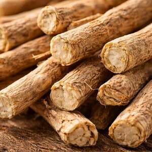 May include: Close-up of a pile of ashwagandha root pieces. The pieces are cylindrical, with a light brown, textured exterior and a lighter, fibrous interior. The roots are stacked on a dark wooden surface, showcasing their natural appearance.
