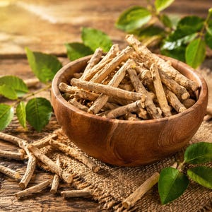 May include: A wooden bowl filled with dried, light brown sticks, possibly herbs or roots, sits on a rustic wooden surface. Green leaves and sprigs are scattered around the bowl, adding a natural element to the composition. The lighting is warm and inviting.