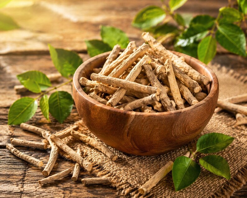 May include: A wooden bowl filled with dried, light brown sticks, possibly herbs or roots, sits on a rustic wooden surface. Green leaves and sprigs are scattered around the bowl, adding a natural element to the composition. The lighting is warm and inviting.
