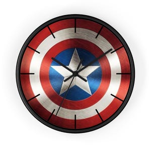 Puede incluir: Reloj de pared redondo con un diseño inspirado en el escudo del Capitán América. La esfera del reloj tiene una combinación de colores rojo, blanco y azul con una estrella blanca central. El reloj tiene un marco negro y manecillas negras.