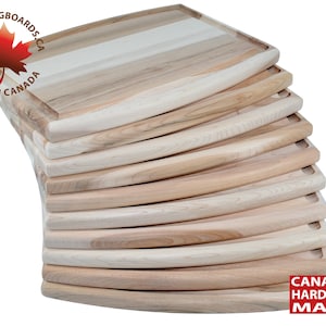 May include: A stack of 10 wooden chopping boards made from Canadian hardwood maple. The boards are all the same size and shape, and they have a slightly curved edge. The boards are stacked on top of each other, with the top board being the most visible. The boards are all a light brown colour, and they have a natural wood grain.