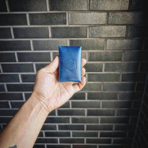 May include: A small, blue leather card holder with the text "Fika's" embossed on the front.